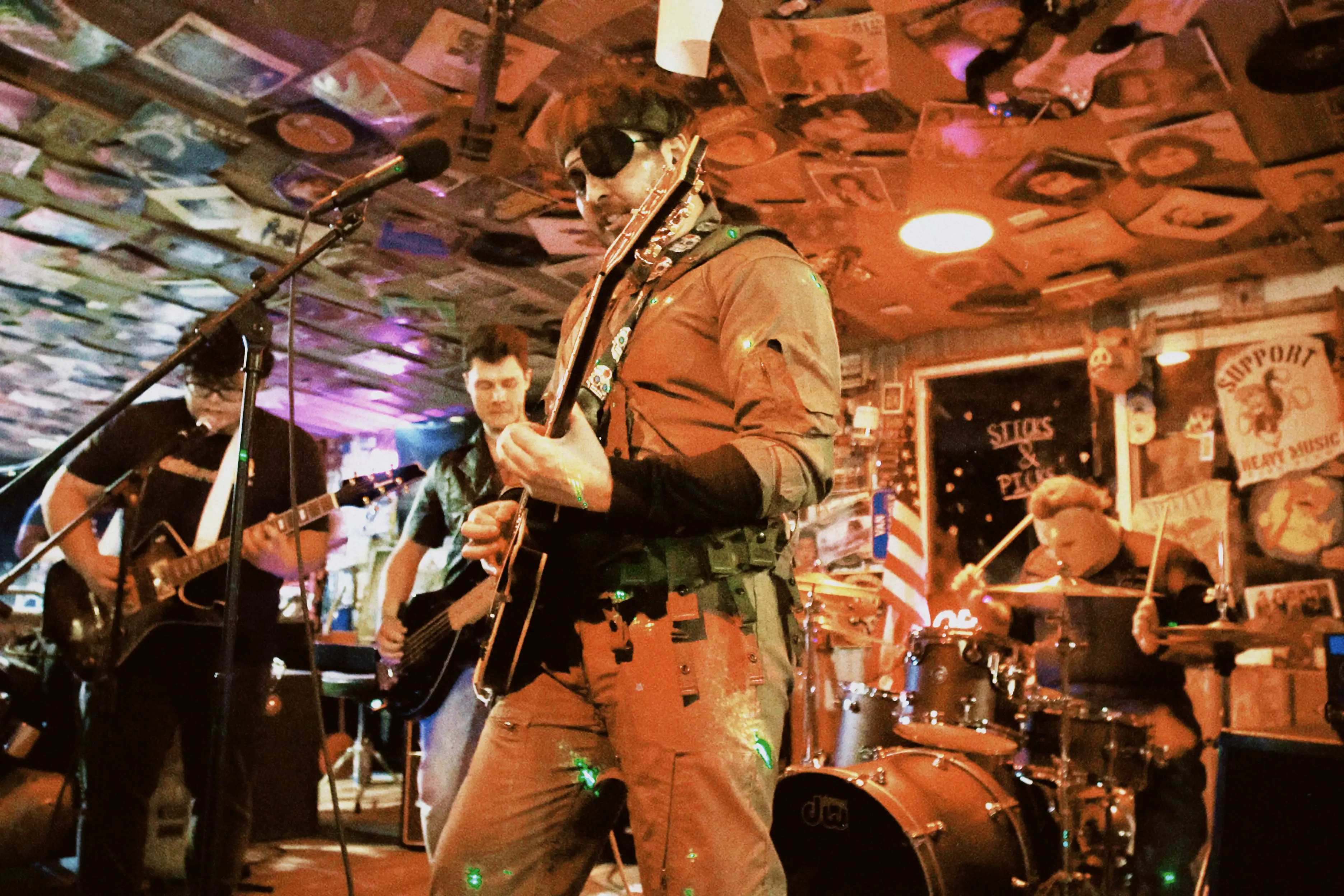 A strange man dressed as Solid Snake plays guitar while a man dressed as Michael Myers plays drums behind him. A guitar player and bass player perform in the background.